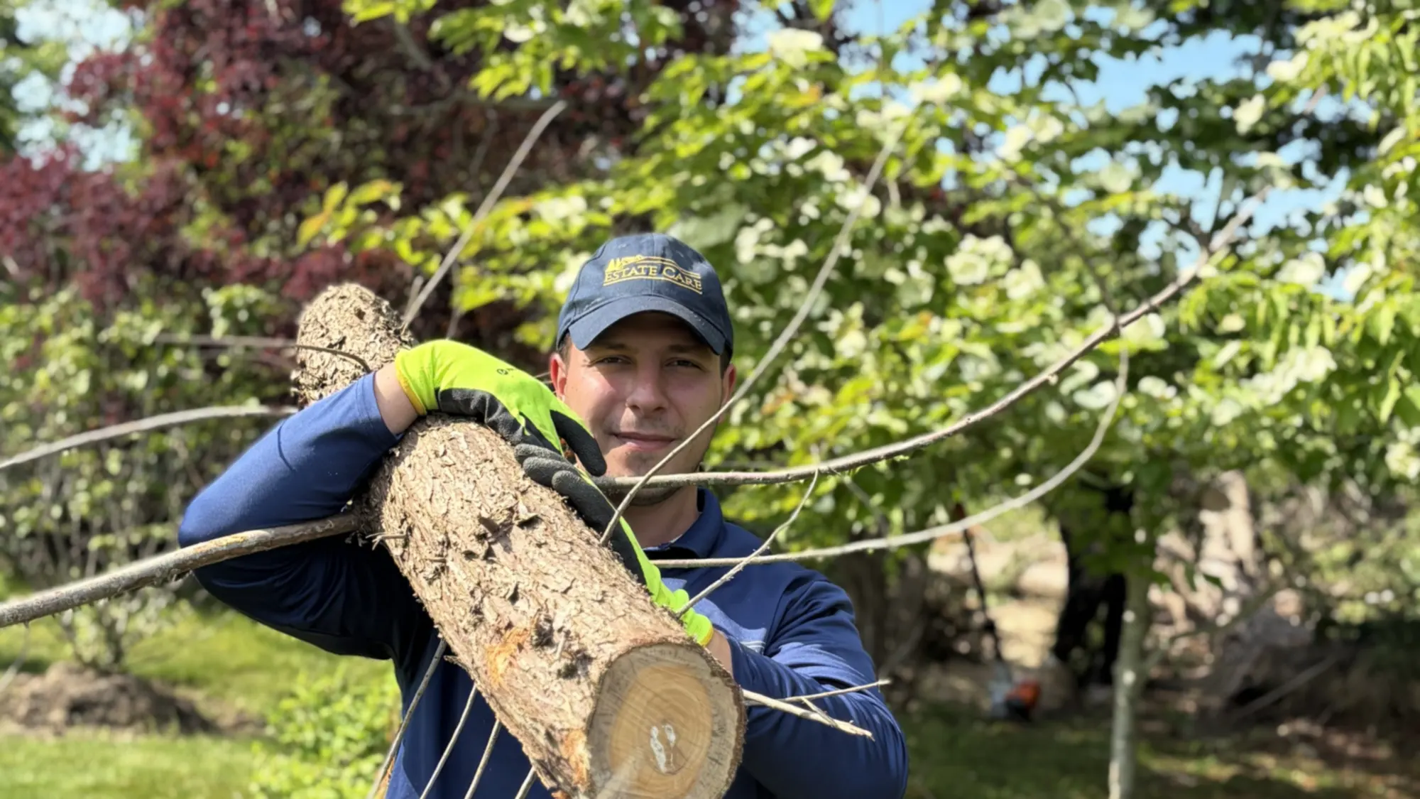 Crew member carrying a cut log clear of a mown lawn