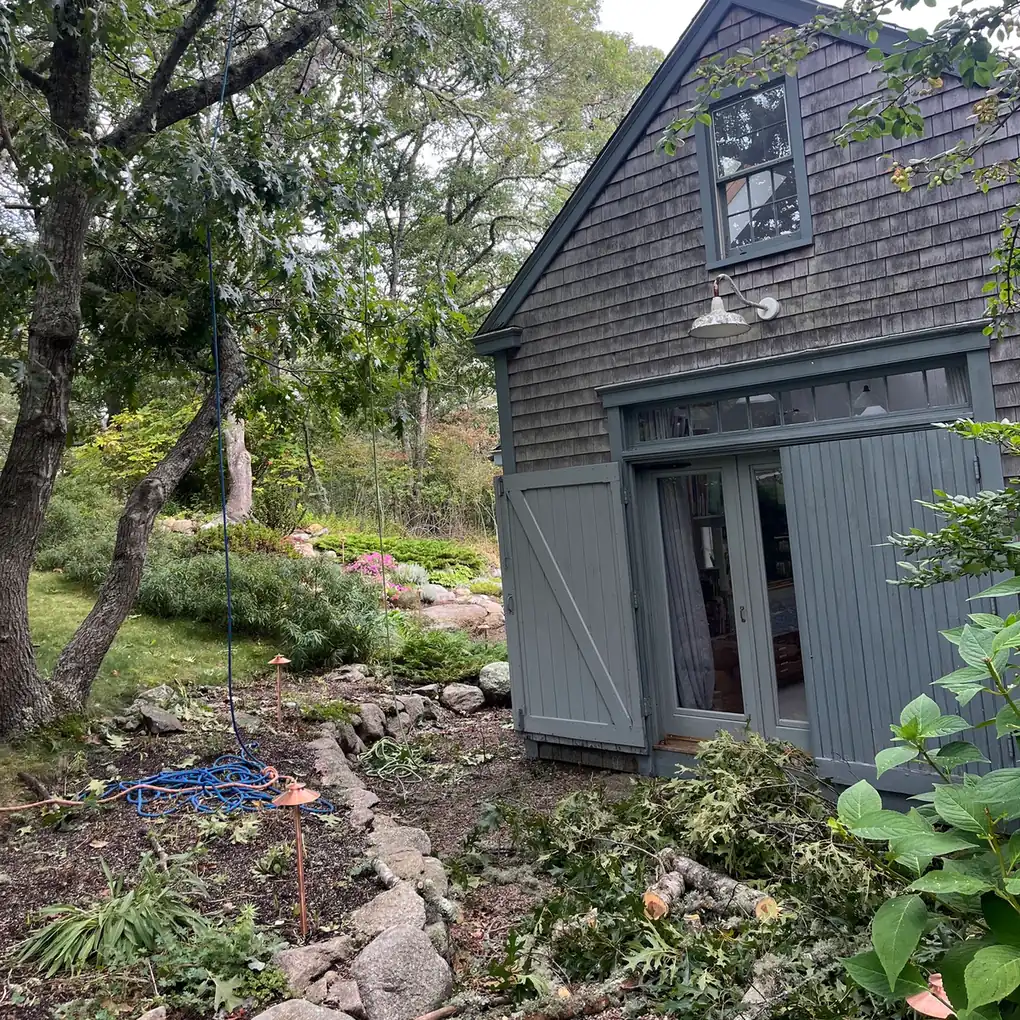 Garden path with stone edging beside a barn, with rope and cut branches